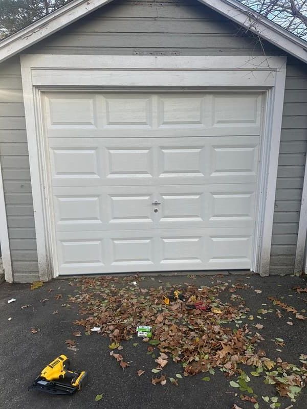 Newly installed white raised-panel single garage door on detached residential garage
